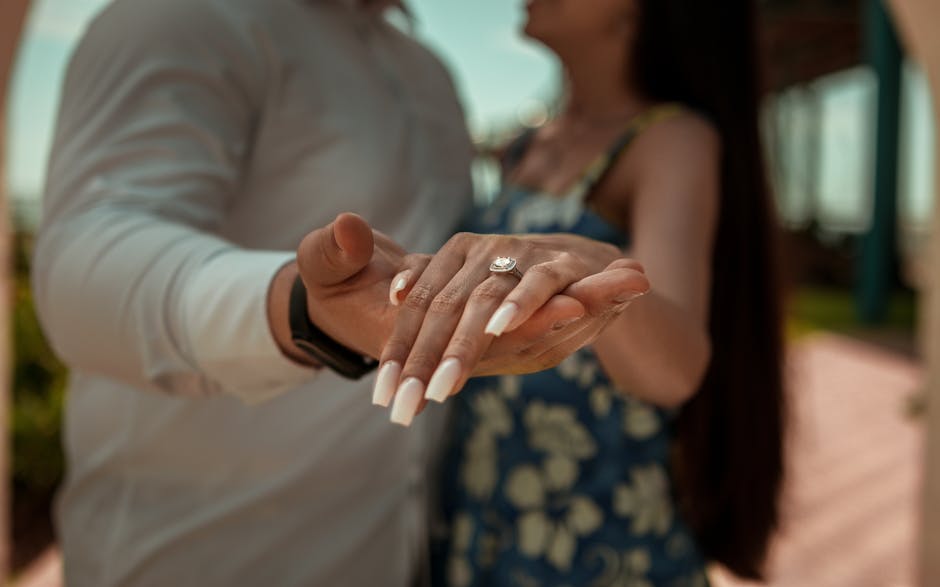 A couple celebrating their engagement, showing a diamond ring on her hand, with a blurred background.